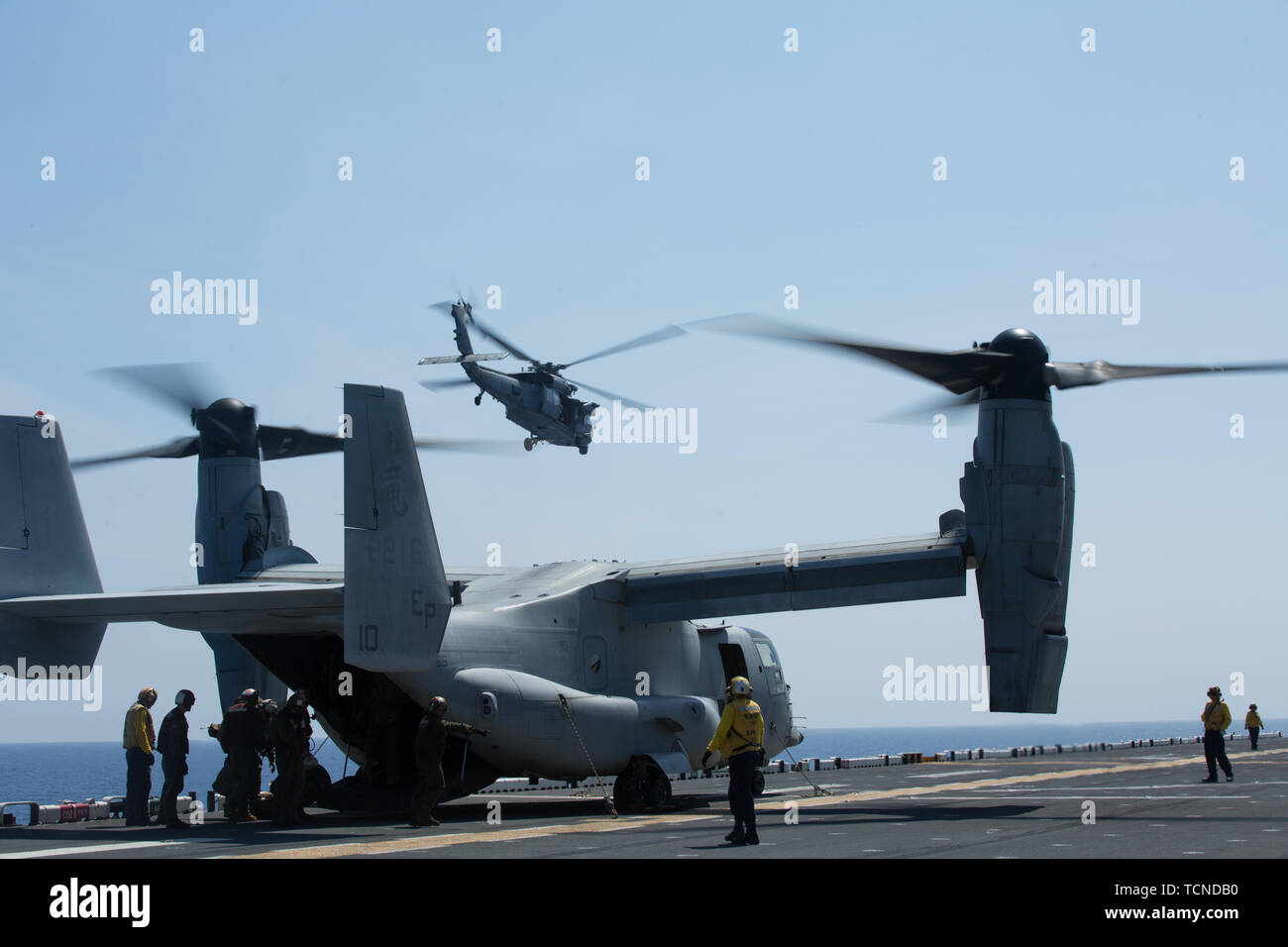 An MH-60S Seahawk takes off as Marines and Sailors with the 31st Marine Expeditionary Unit and the amphibious assault ship USS Wasp (LHD 1) unload supplies from an MV-22B Osprey tiltrotor aircraft while underway in the Philippine Sea, June 5, 2019. The 31st Marine Expeditionary Unit, the Marine Corps` only continuously forward-deployed MEU, provides a flexible and lethal force ready to perform a wide range of military operations as the premier crisis response force in the Indo-Pacific region. (Official U.S. Marine Corps photo by Lance Cpl. Kenny Nunez Bigay) Stock Photo